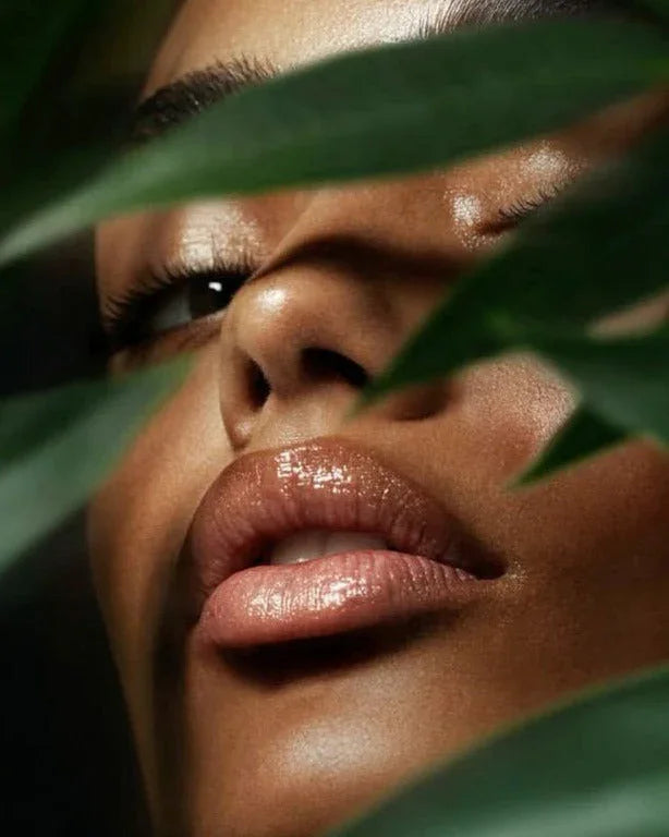 Close-up of woman's glossy lips and face with smooth skin, partially obscured by green leaves